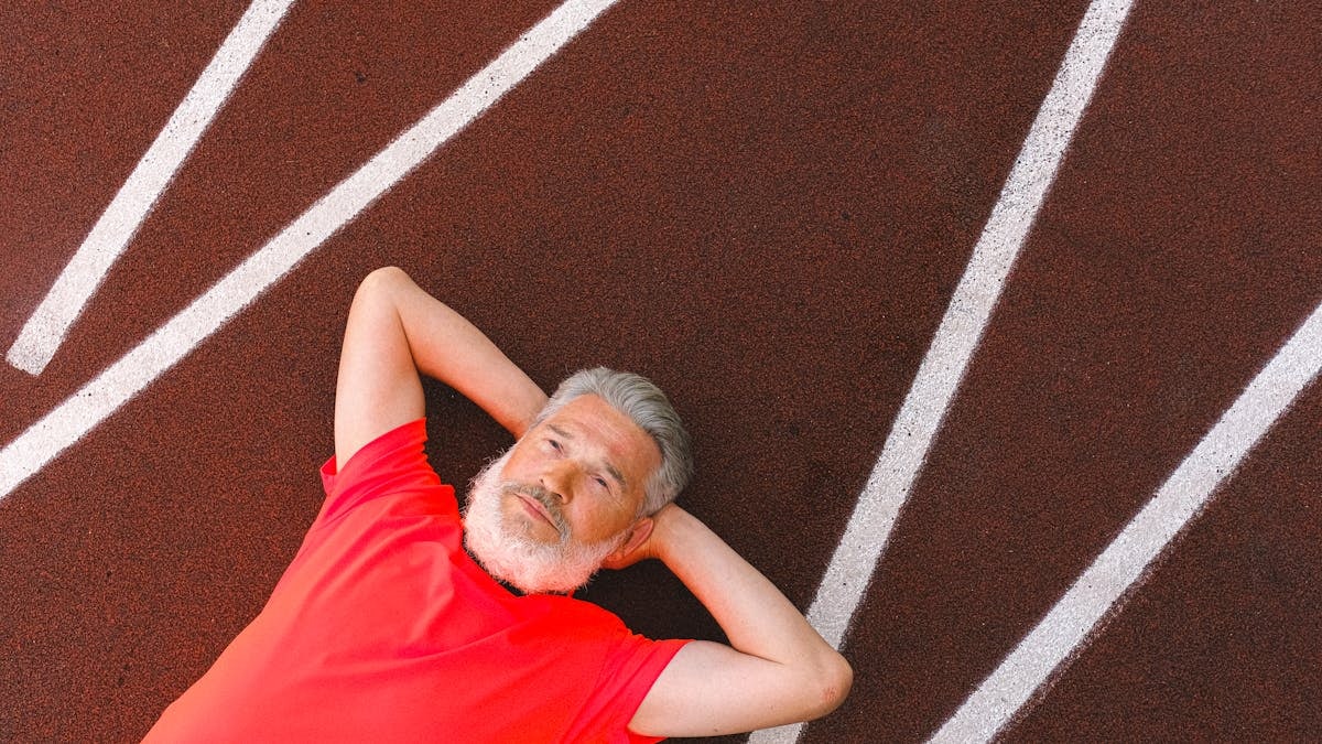 From above of calm elderly female with gray hair lying and relaxing on racetrack in stadium