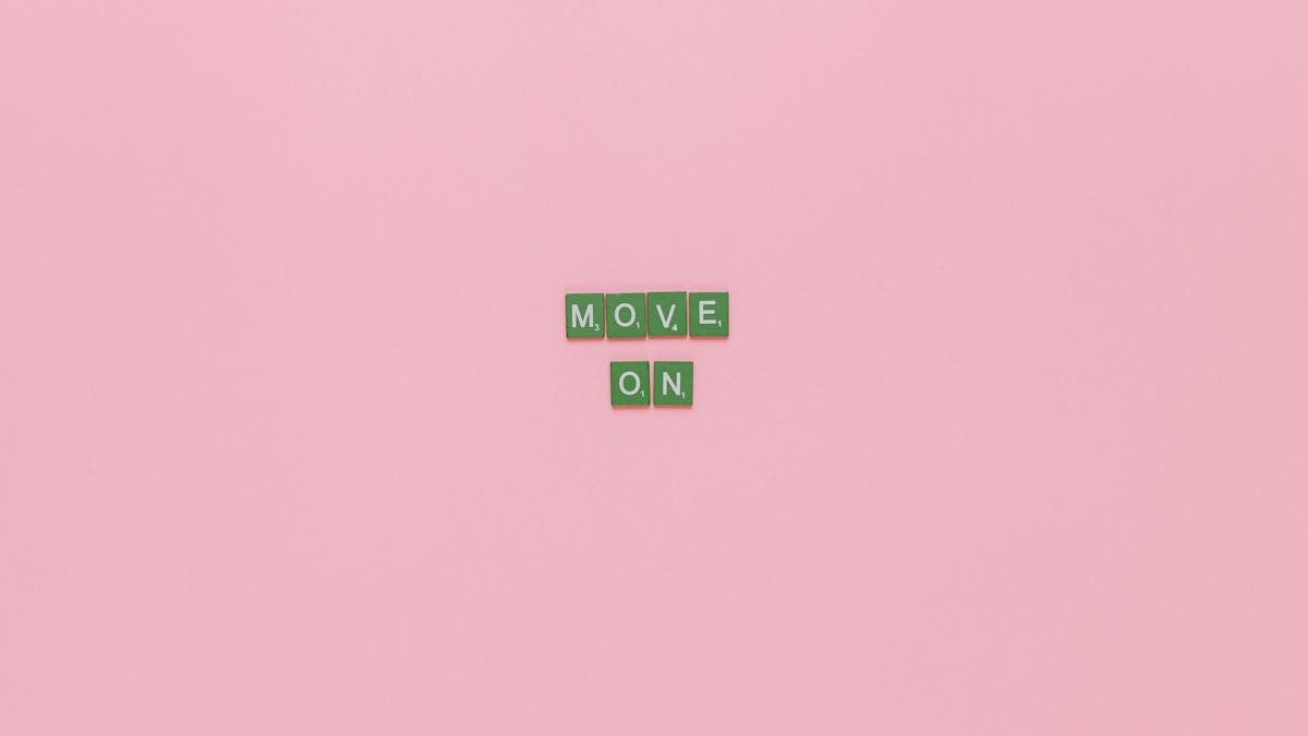 Inspirational text "Move On" spelled with green tiles on a pink background. Minimalist design, perfect for motivation.